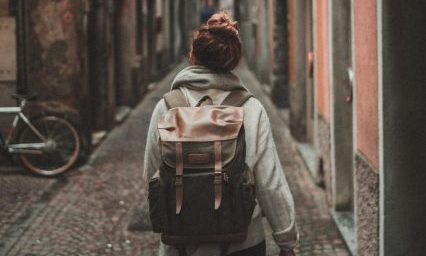 Rückansicht einer Frau mit Rucsack, die einer Straße folgt.